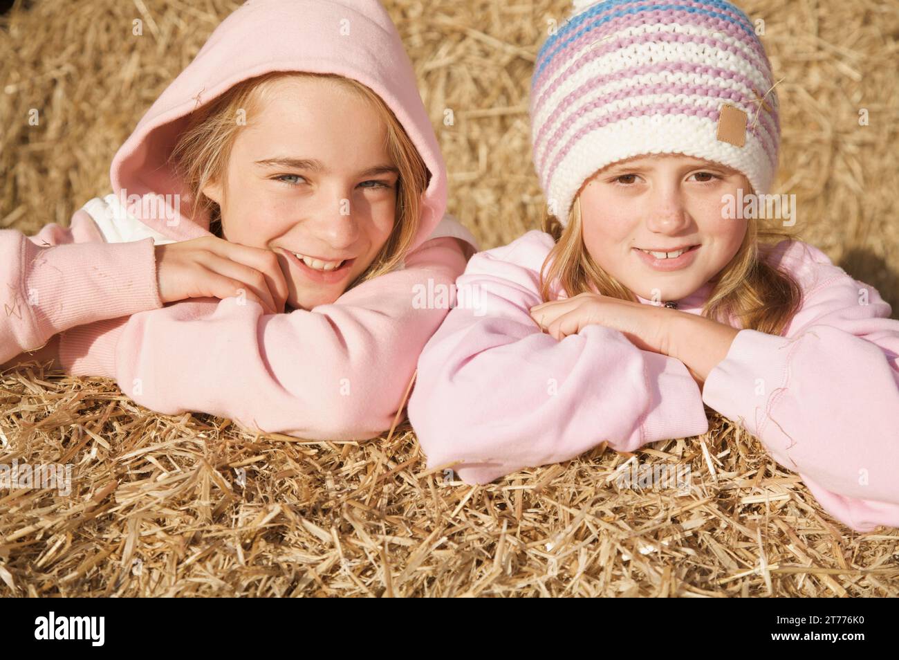 Two young girls leaning on bale of hay smiling Stock Photo