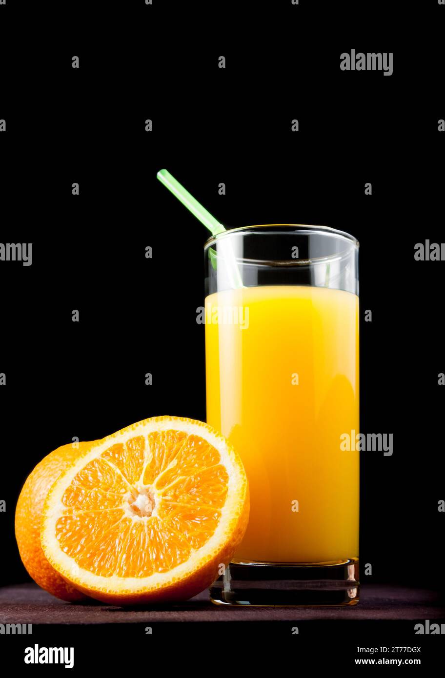 full glass of orange juice with straw near half orange on black background Stock Photo