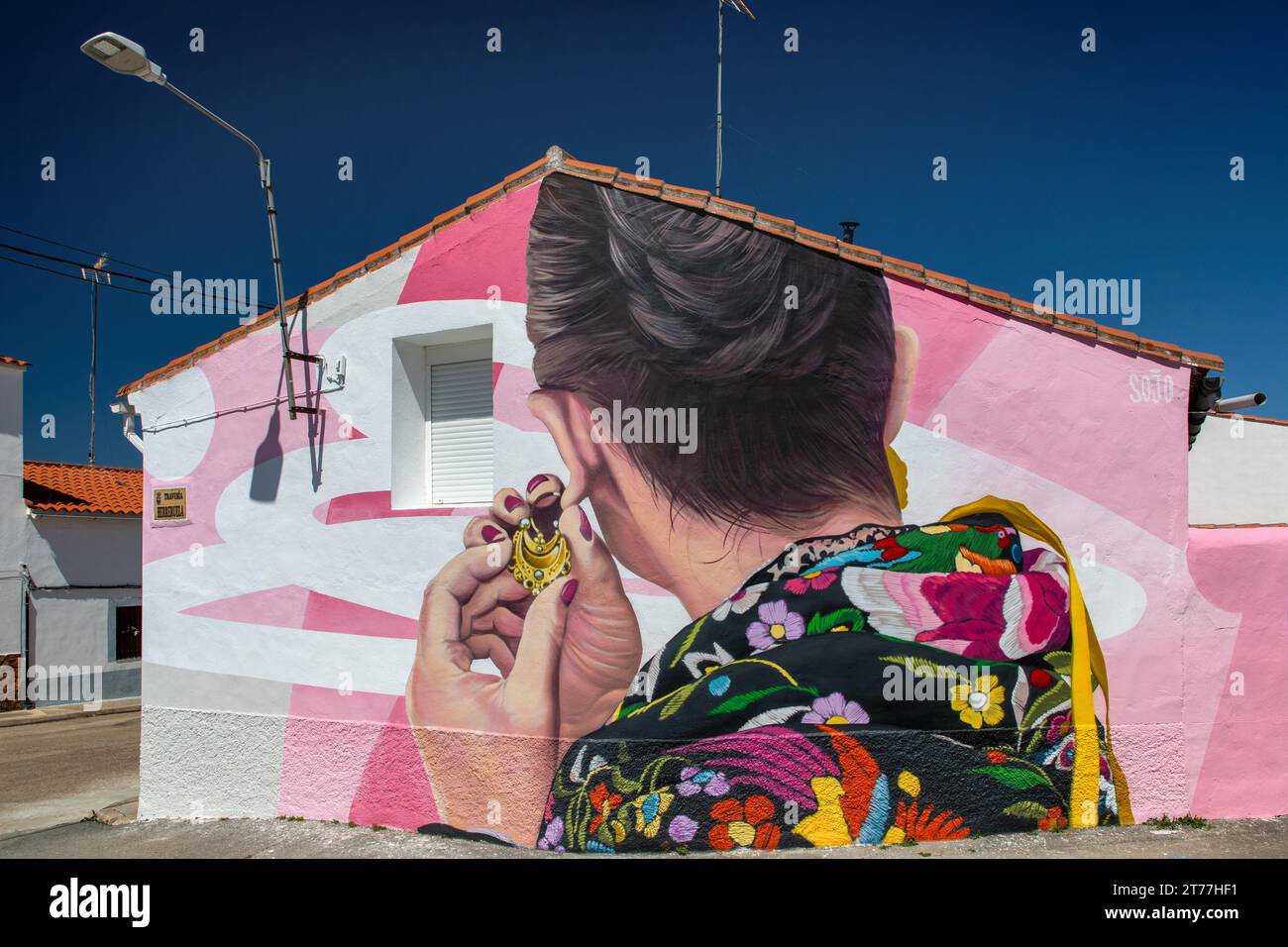 artistically painted house wall, woman putting on a traditional earring, Spain, Extremadura, Salorino Stock Photo