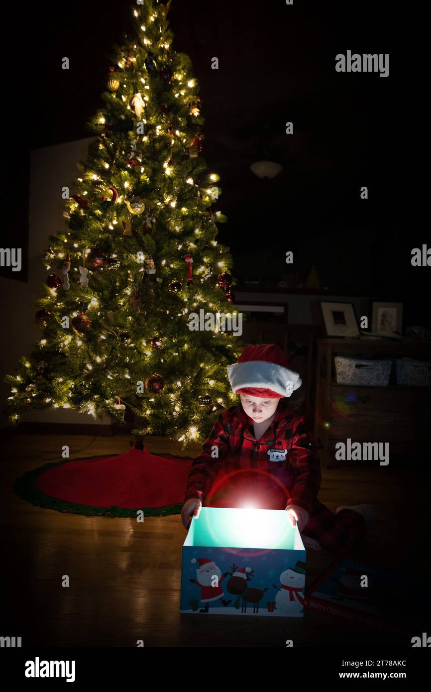 Child opening Christmas gift under Christmas tree Stock Photo