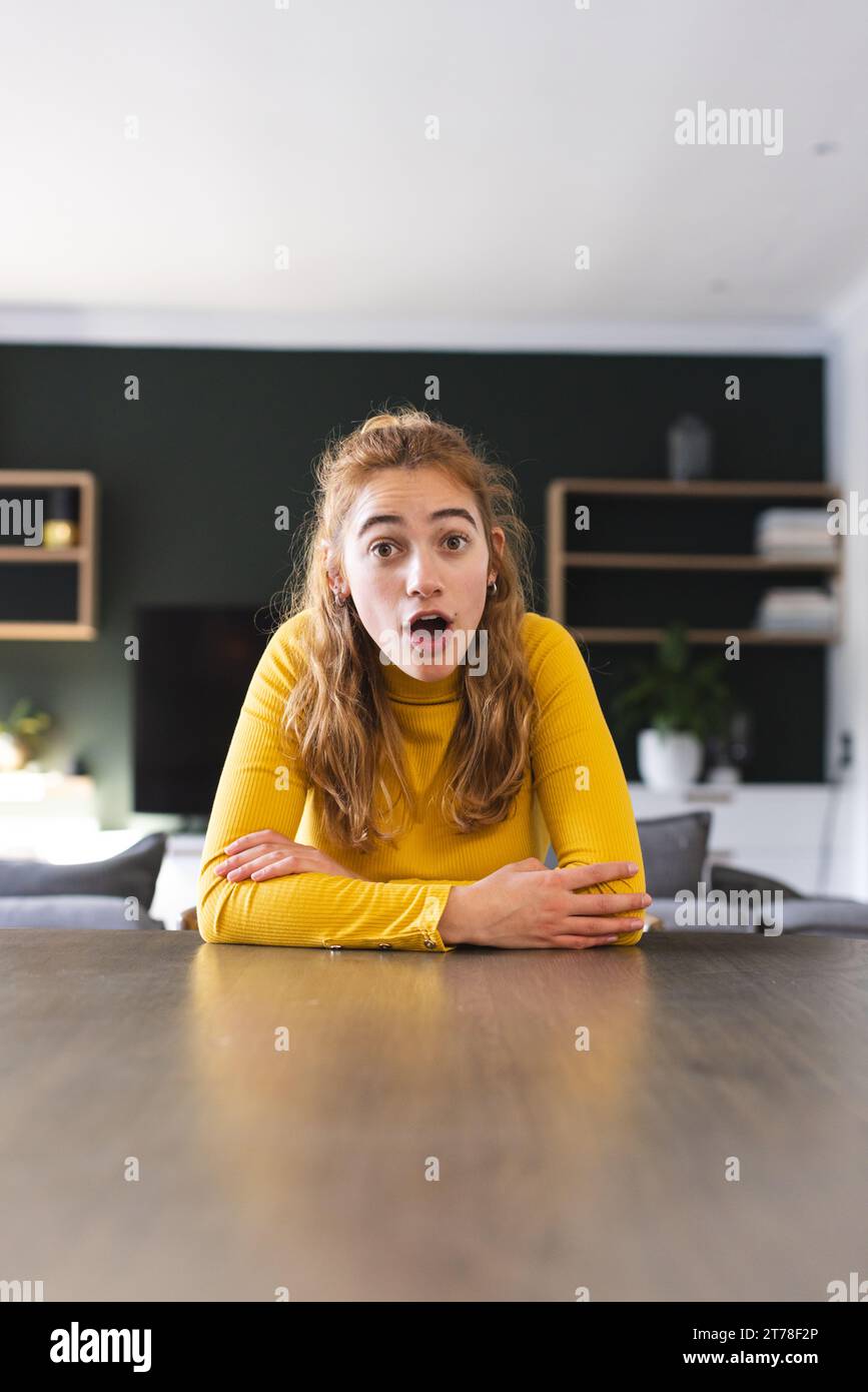 Surprised biracial woman sitting at dining table having video call at