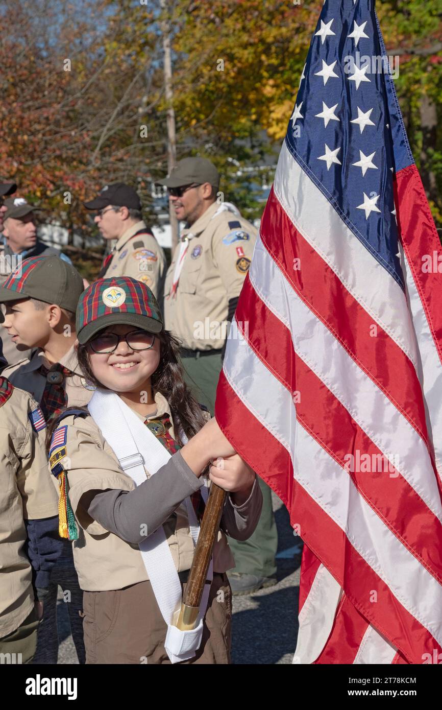 Posed portrait of a very cute girl scout holding a large American flag. Prior to the start of the 2023 Somers Veterans Day Parade in Westchester, NY. Stock Photo