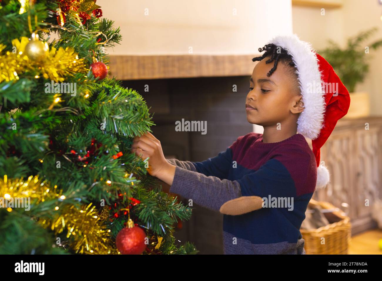 Focused african american boy, wearing christmas hat decorating christmas tree at home, copy space Stock Photo