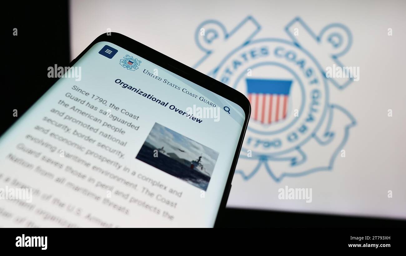 Mobile phone with website of United States Coast Guard (USCG) in front of seal. Focus on top-left of phone display. Stock Photo