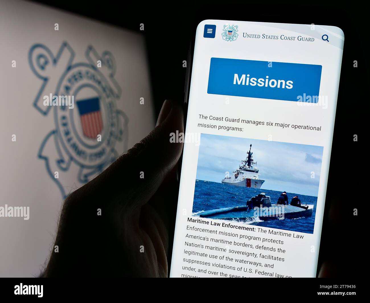 Person holding cellphone with webpage of United States Coast Guard (USCG) in front of seal. Focus on center of phone display. Stock Photo
