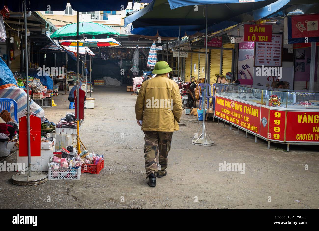 A Vietnamese man in combat trousers and wearing a green army pith helmet walks through the market in Mong Cai, Quang Ninh, Vietnam. Stock Photo