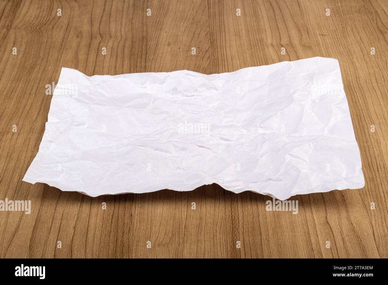 Crumpled sheet of white office paper on a wooden table. Copy space. Stock Photo