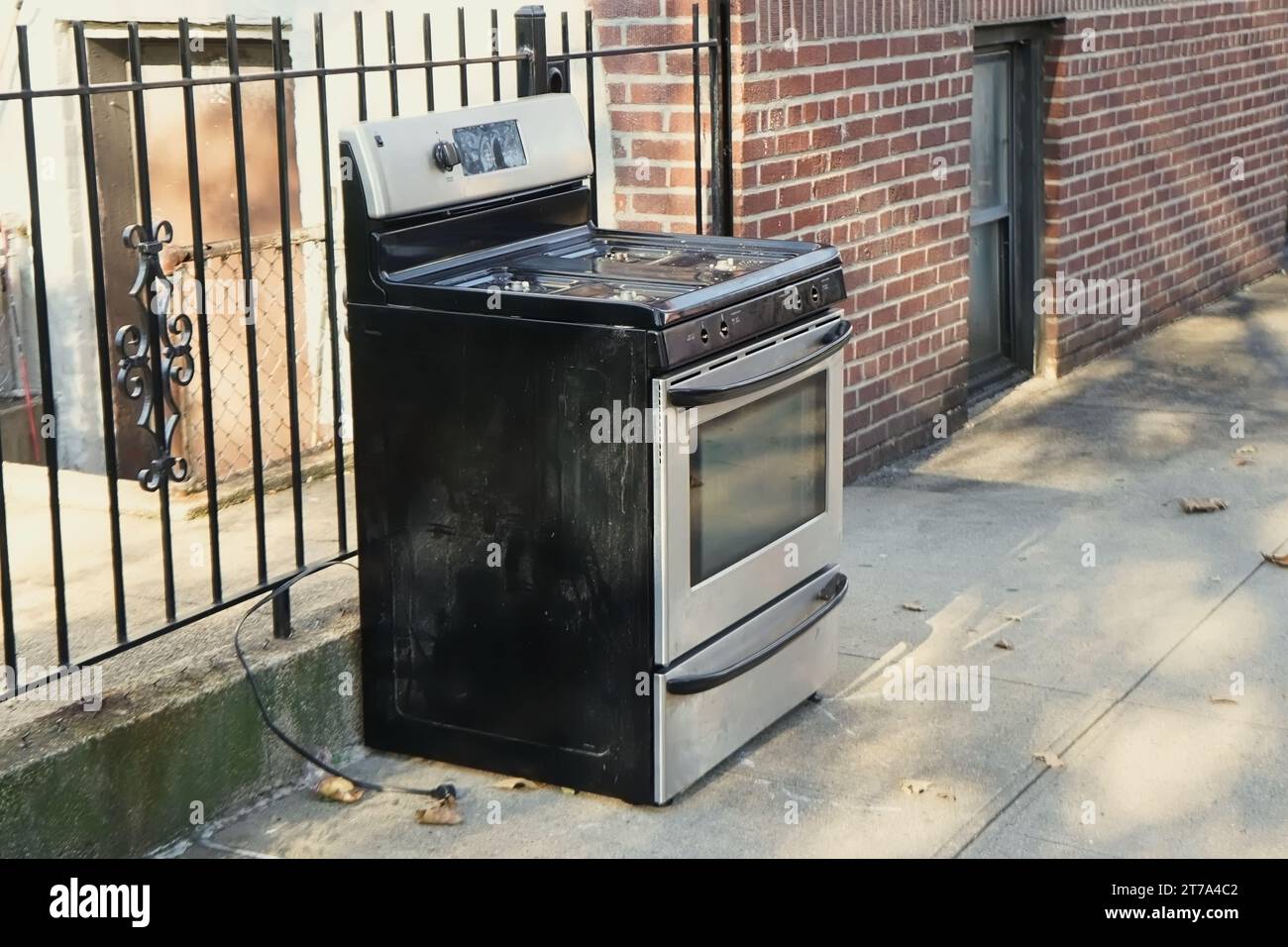 Thrown out used steel stove oven on the city street sidewalk as left as garbage pickup or illegally dumped Stock Photo
