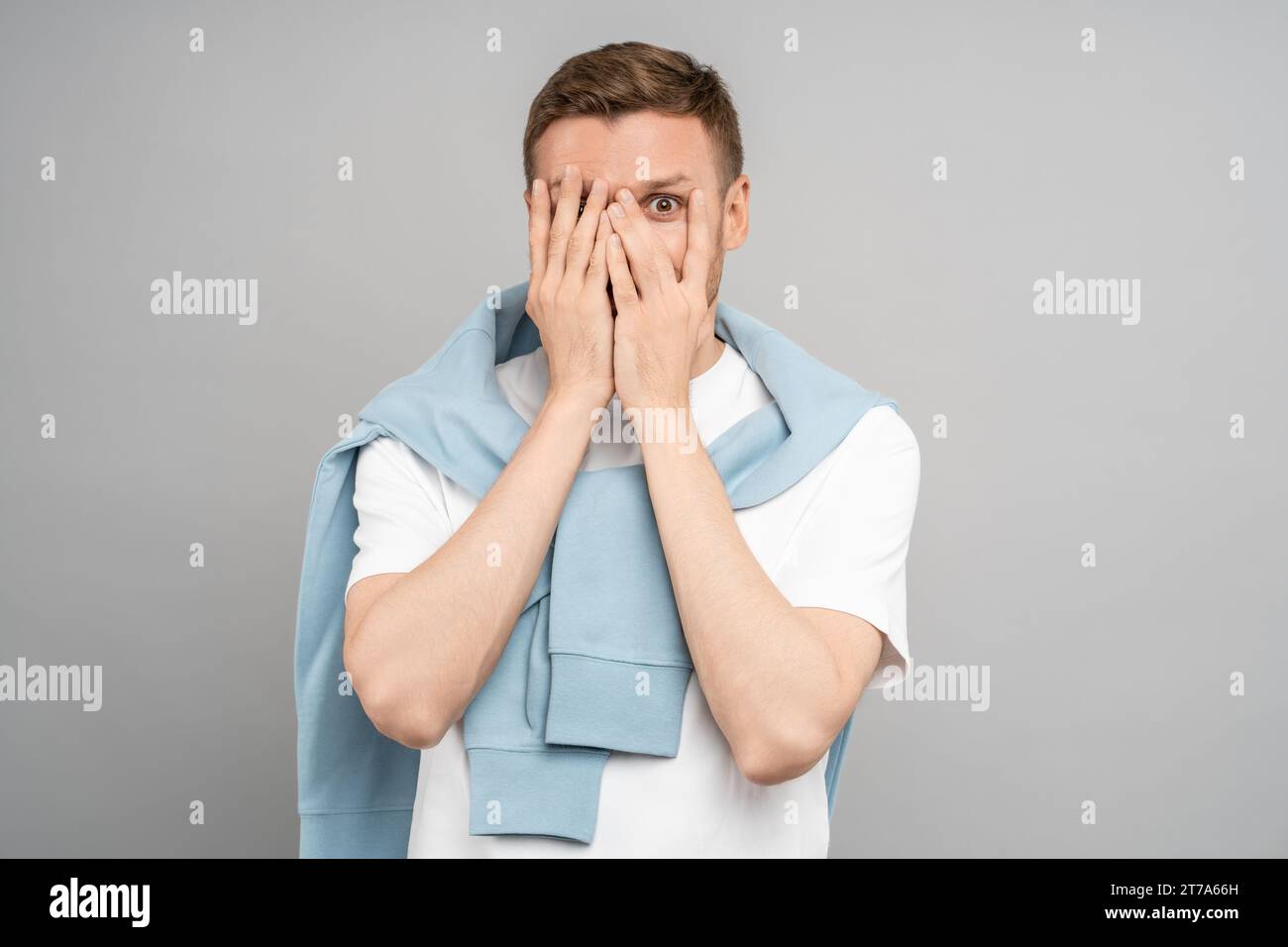 Man looks through fingers. Frightened middle aged guy covers face with