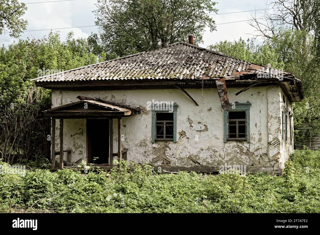 A photo of an old, dilapidated house with a crumbling roof and overgrown vegetation. Stock Photo