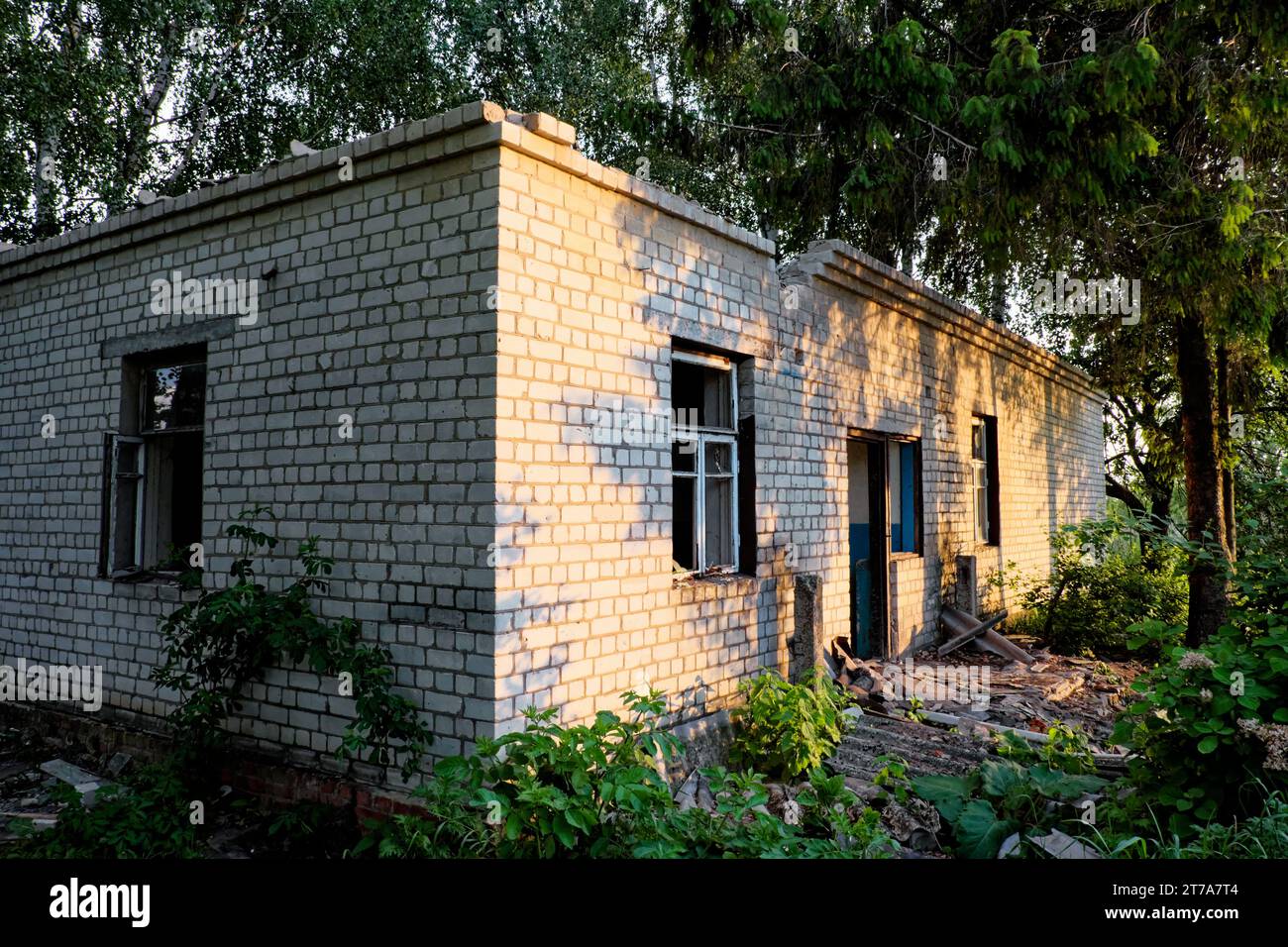 An abandoned brick building with broken windows and overgrown vegetation. Stock Photo
