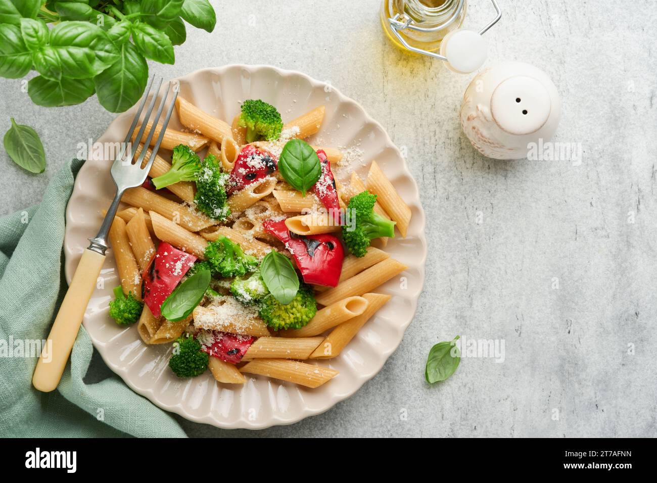 Wholegrain pasta penne with broccoli and red grilled bell pepper and on light grey slate, stone or concrete background. Vegan pasta. Traditional Itali Stock Photo