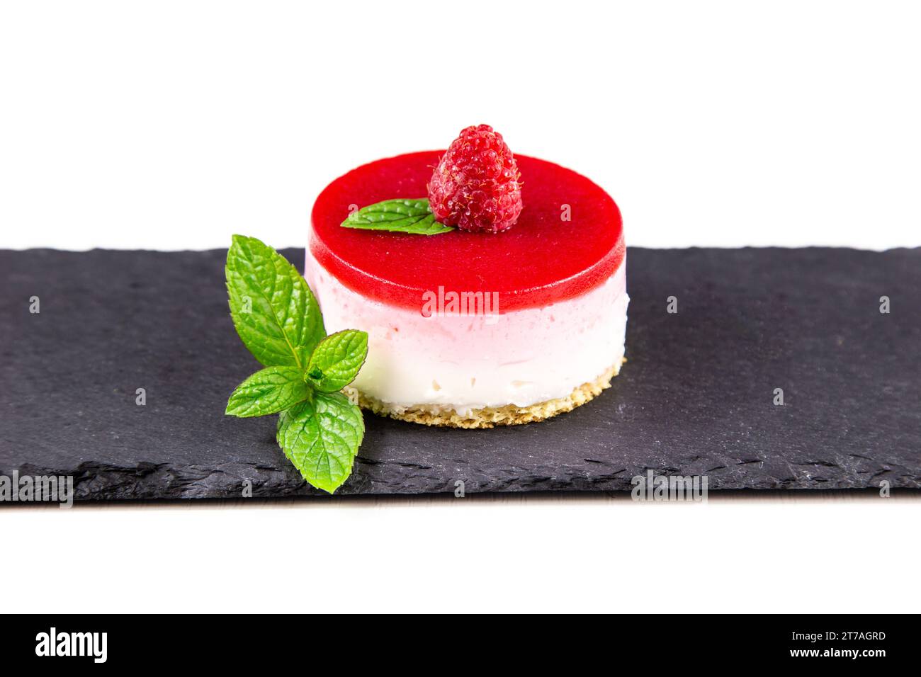 A delicious raspberry cheesecake with fresh raspberries and mint leaves on a black slate plate. Stock Photo