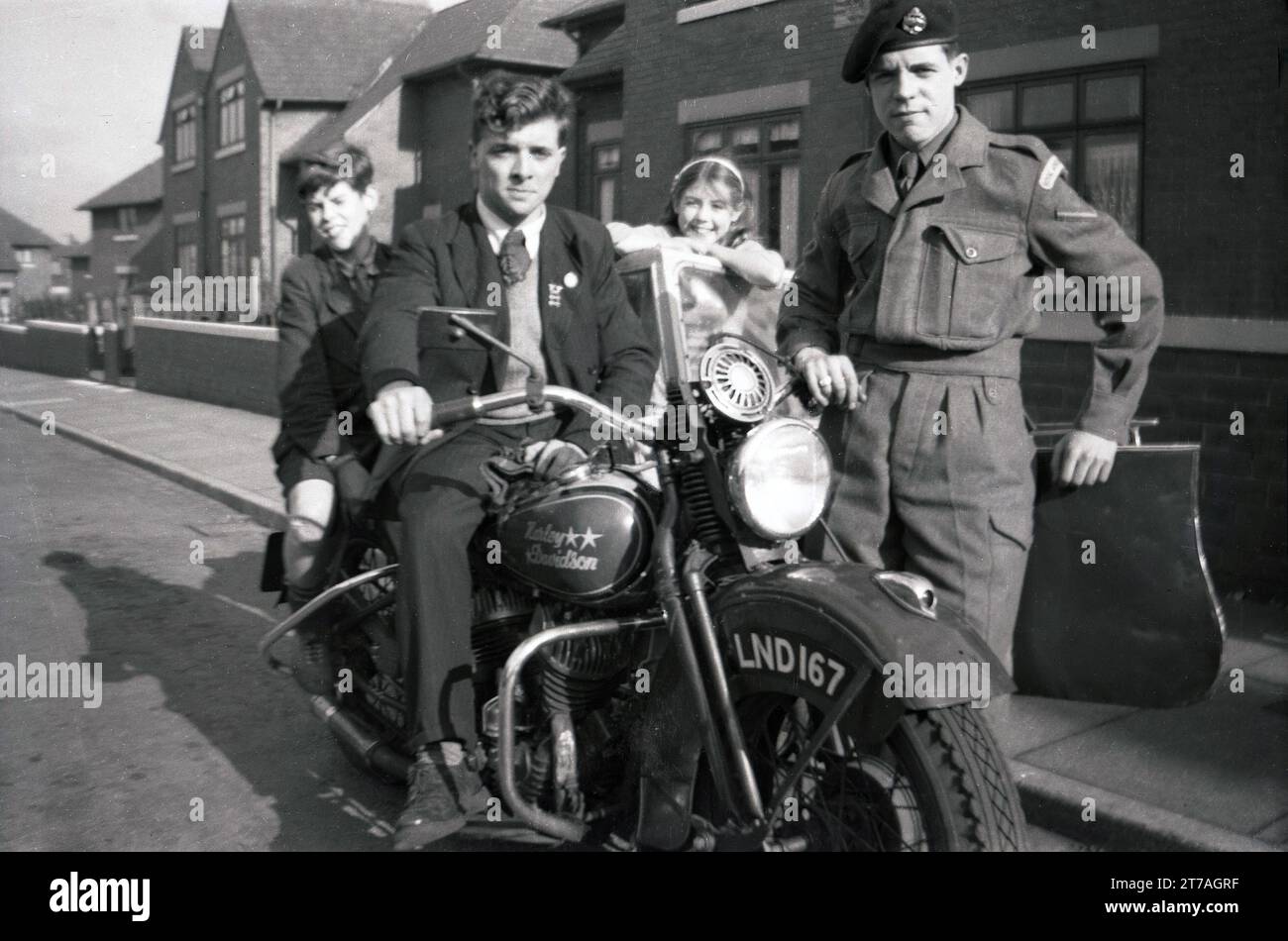 1950s, historical, young man on a Harley Davidson motorcycle + sidecar of the era, probably owned by an army man standing next to him, England, UK. A younger boy sits behind him and a girl stands in the sidecar Stock Photo