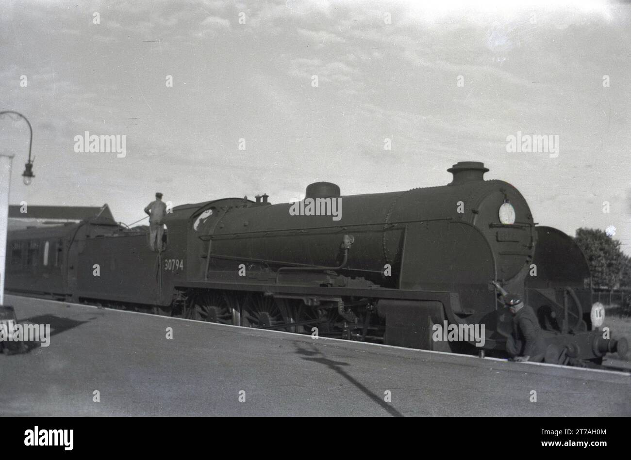 1950s, historical, a steam locomotive of the era, 30794, waiting at a railway platform, England, UK. The 4-6-0 King Arthur Class locomotive entered service in 1926 for Southern Railways (794) before being renumbered 30794 when British Railways was formed in 1949. She was withdrawn in 1960. Stock Photo