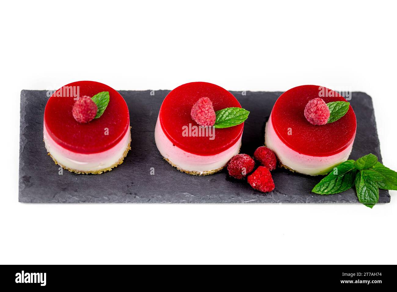 A delicious raspberry cheesecake with fresh raspberries and mint leaves on a black slate plate. Stock Photo