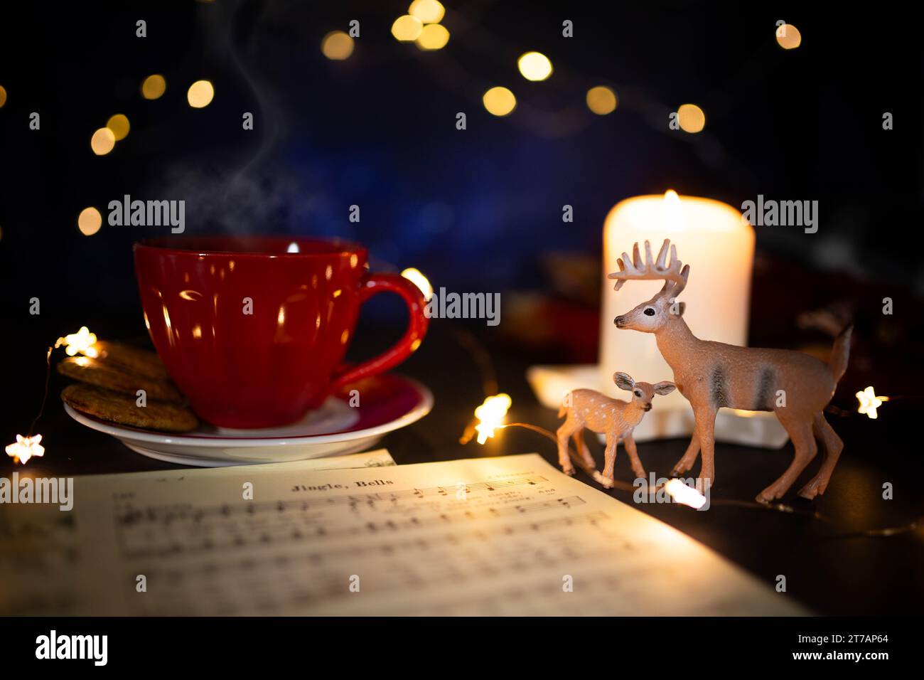 Warm toned Christmas still life with red coffee cup, carol music sheet and deer figurines in