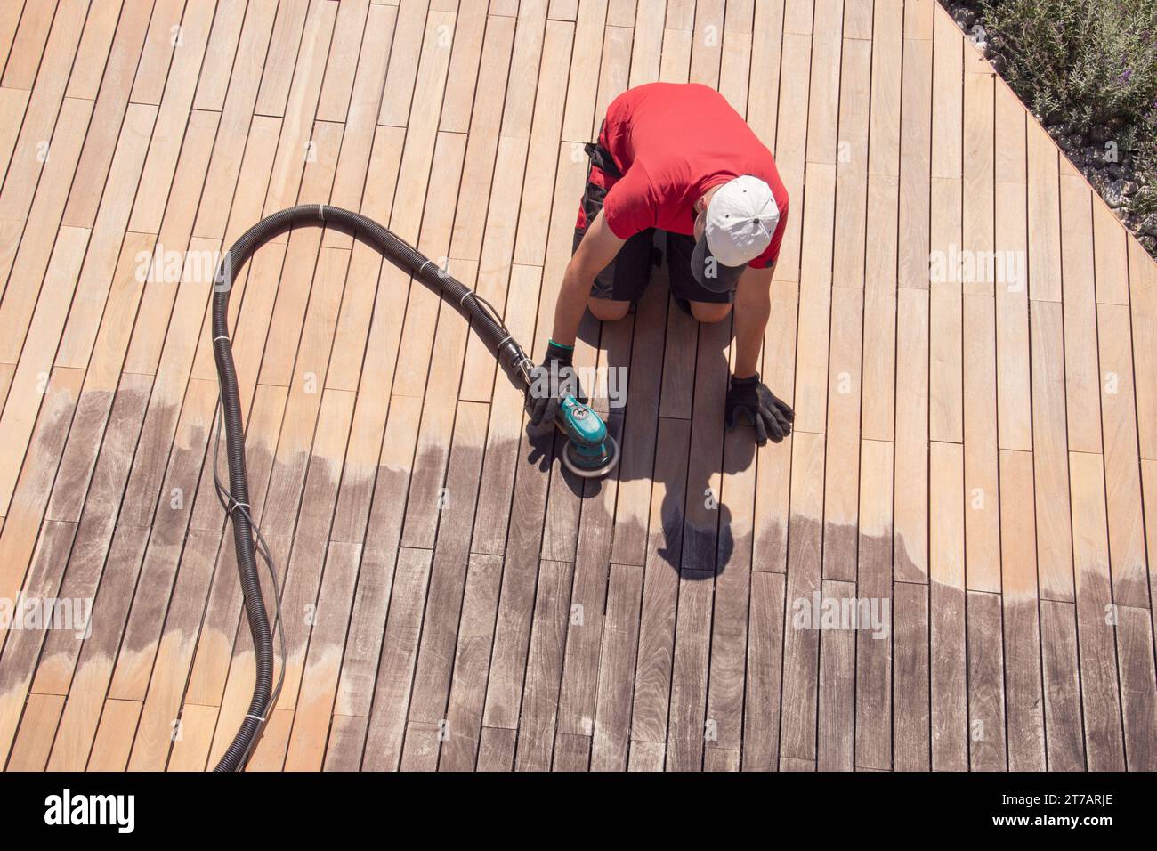 Man sanding wood terrace on the sun with orbital power sander, deck