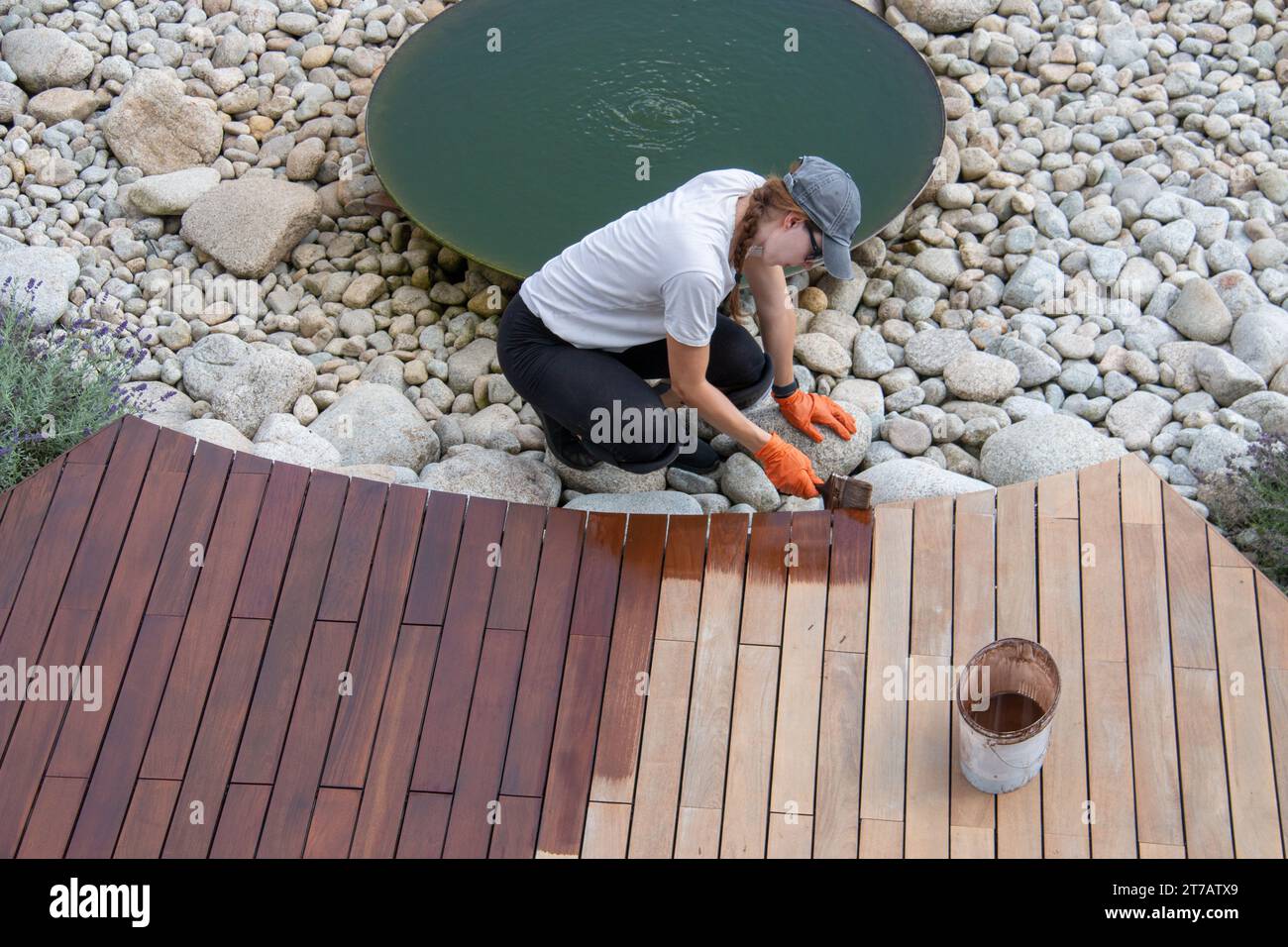 Female worker applying deck protection sealer, house terrace wood staining concept, high angle