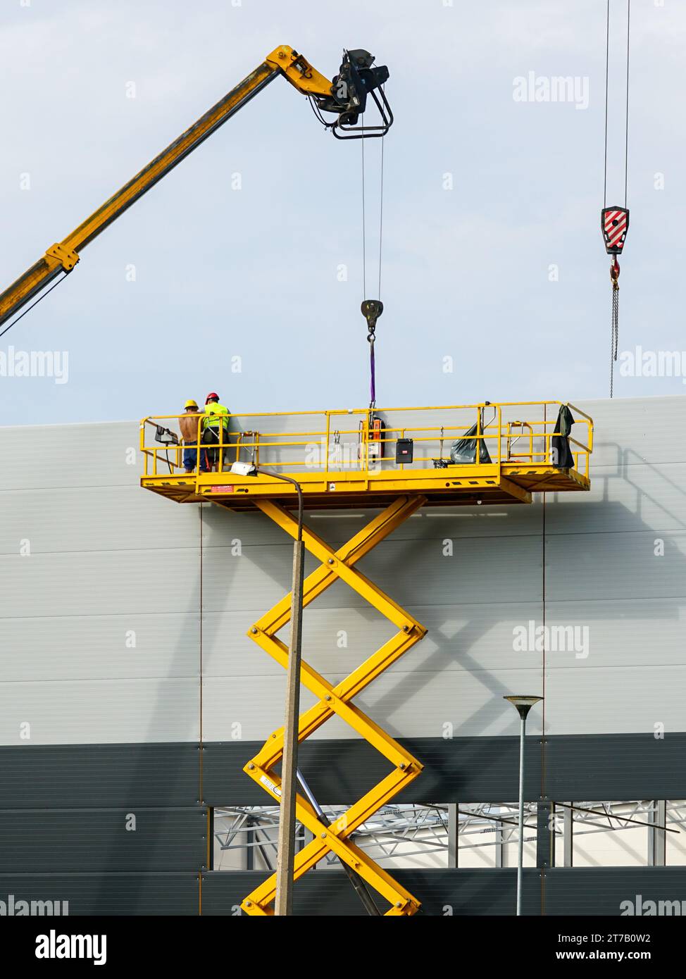 Sandwich panels wall assembly using telescopic boom crane and yellow self propelled scissor lift platform Stock Photo