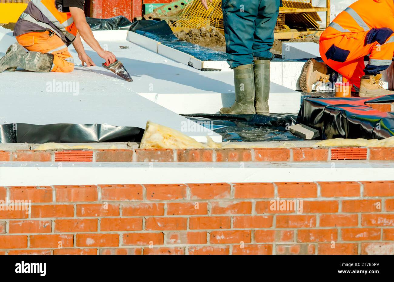 Builder placing polystyrene insulation boards on waterproofing membrane