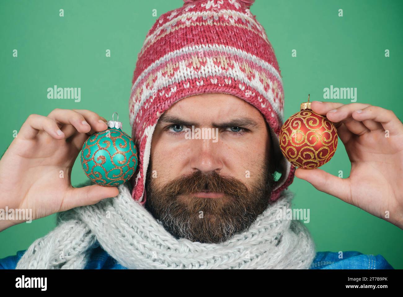 Bearded man in hat and scarf with colored Christmas tree toy. Holiday decorations and ornaments. Christmas or New Year holidays. Serious man with Stock Photo