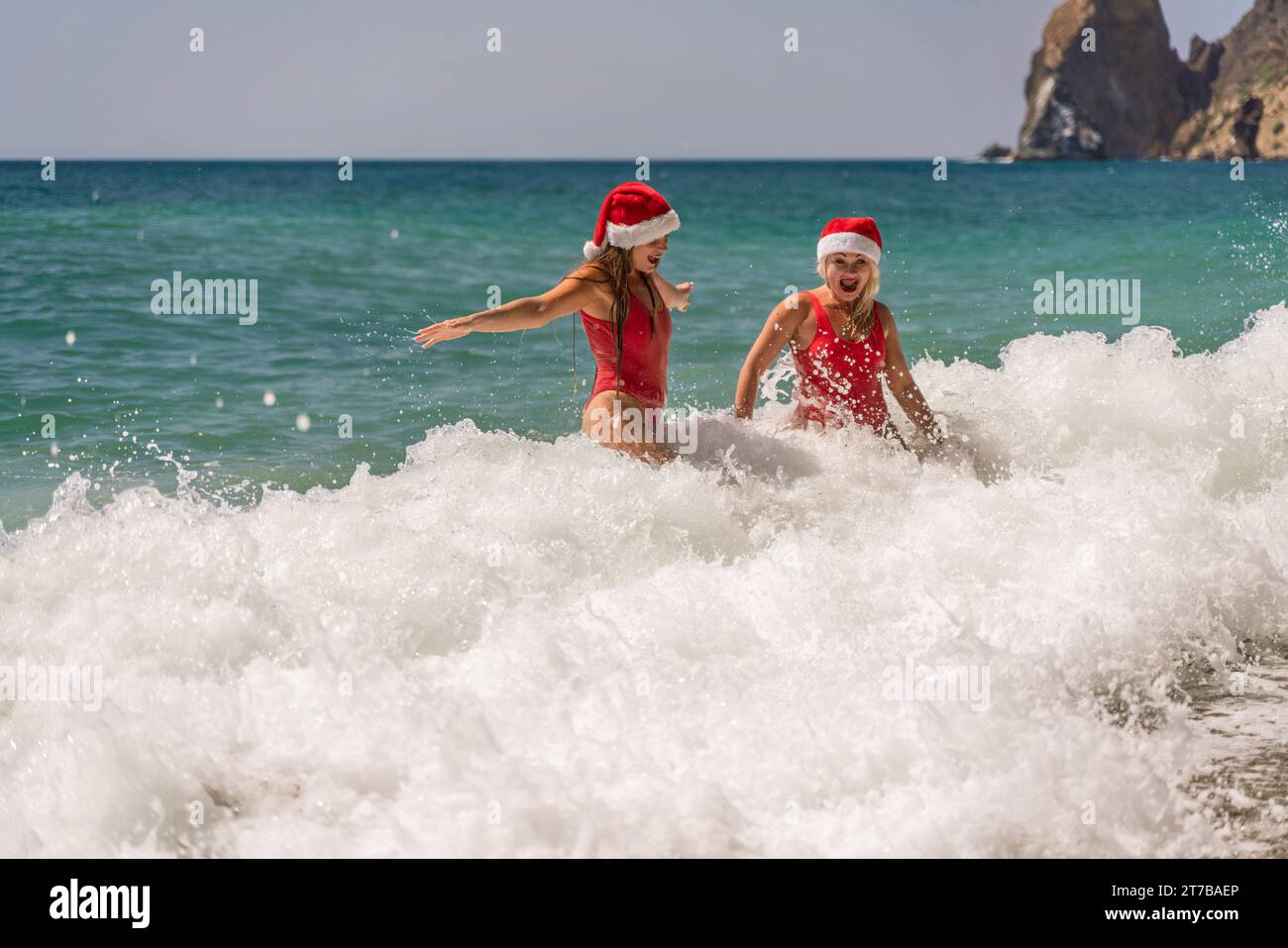Women in Santa Claus hats run into the sea dressed in red swimsuits ...
