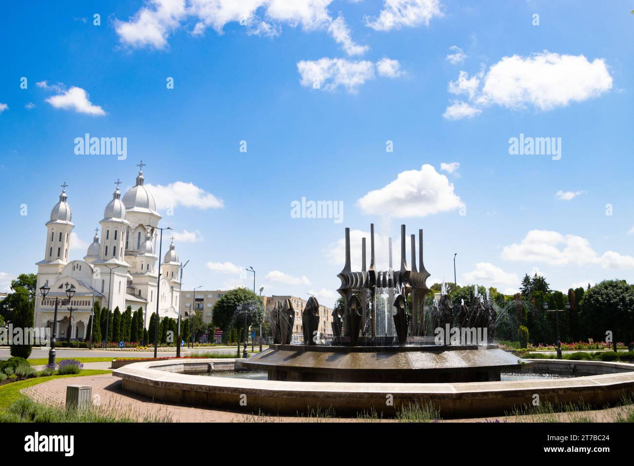 Water fountain and a church in the background on a summer day in the center of Carei, Satu Mare county, Romania Stock Photo