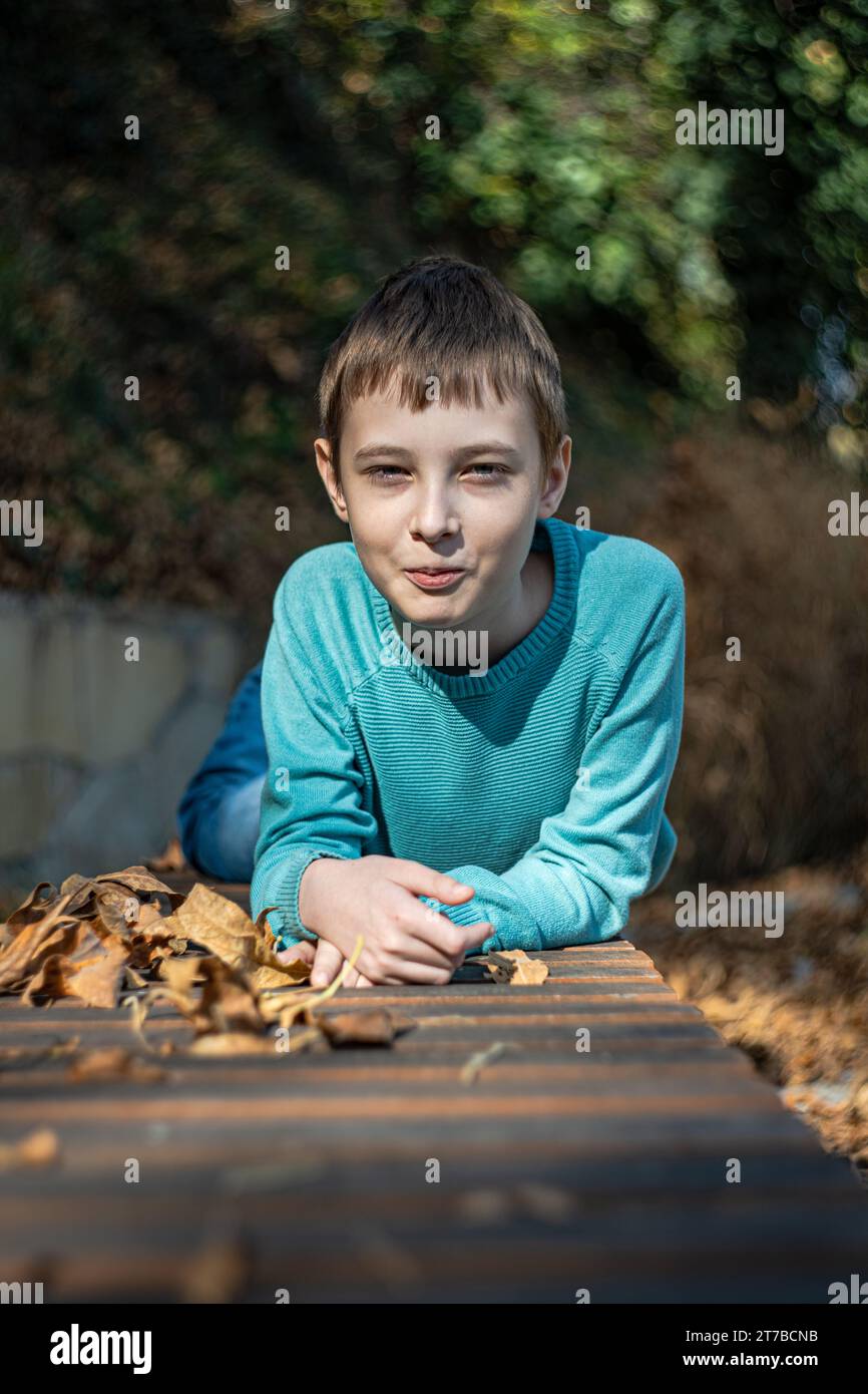 Portrait of a smiling boy lying on a park bench amongst autumn leaves ...