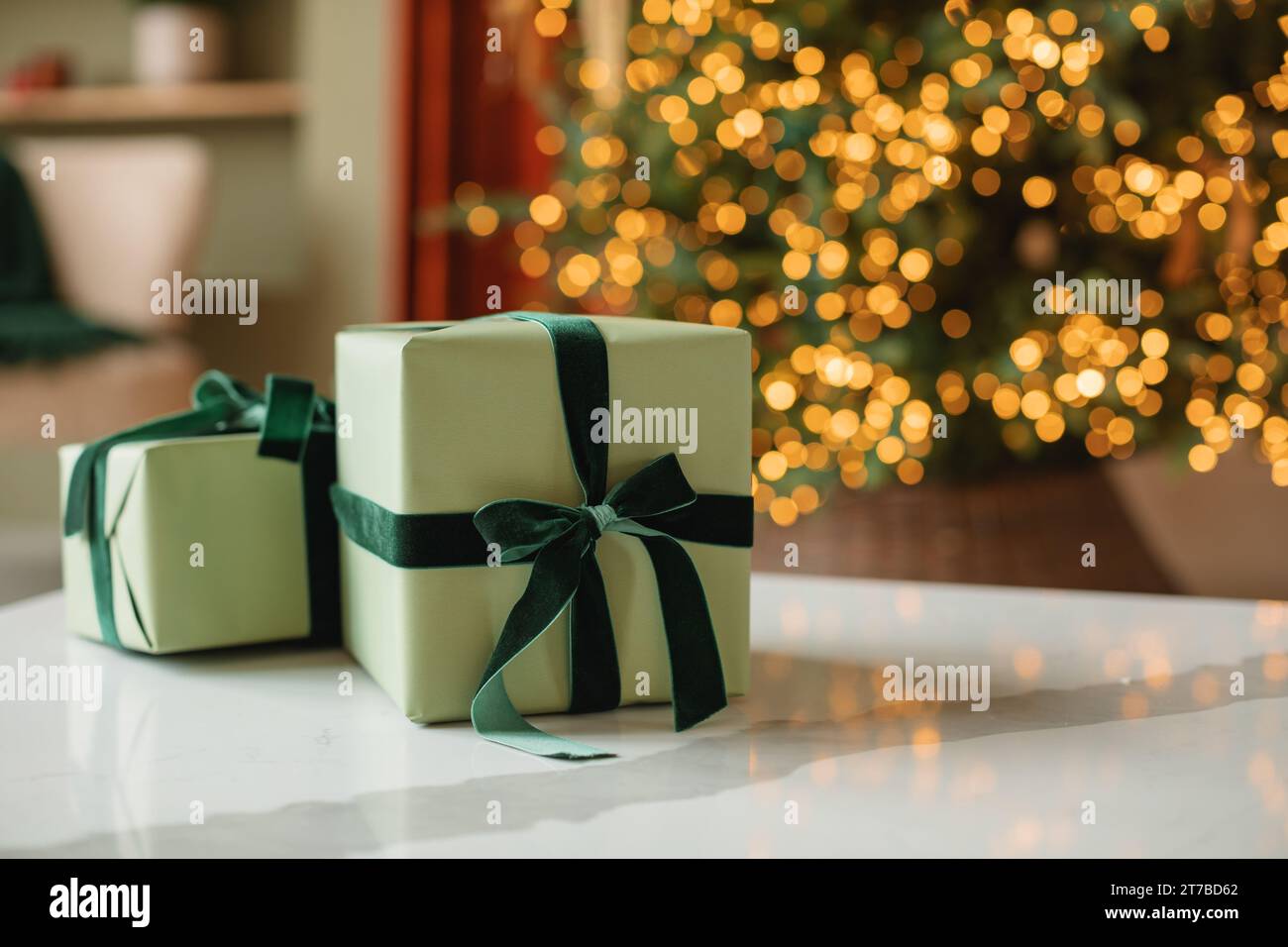Stack of wrapped Christmas gifts in front of an illuminated Christmas tree in a living room Stock Photo
