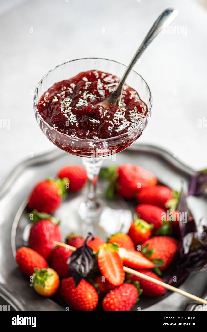 Close-up of fresh strawberries and purple basil on a pewter plate with a bowl of homemade jam Stock Photo