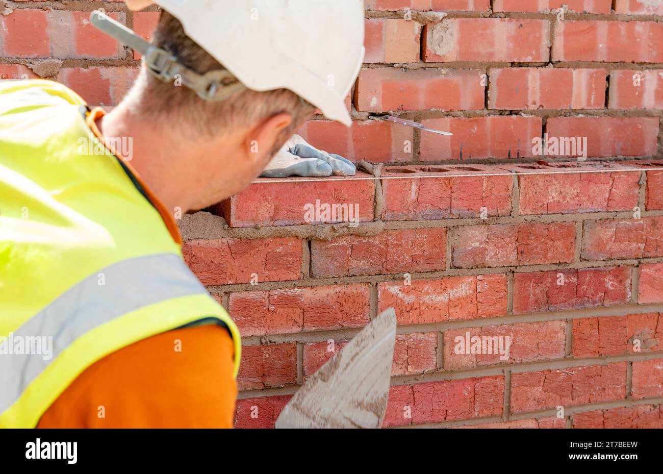 Bricklayers laying bricks on mortar Bricklayer making finishing touches to the brick wall and