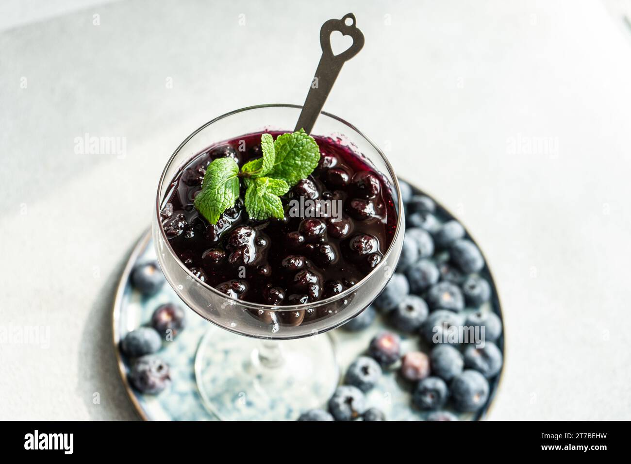 Close-up of a glass of blueberry jam with mint on a plate with fresh blueberries Stock Photo