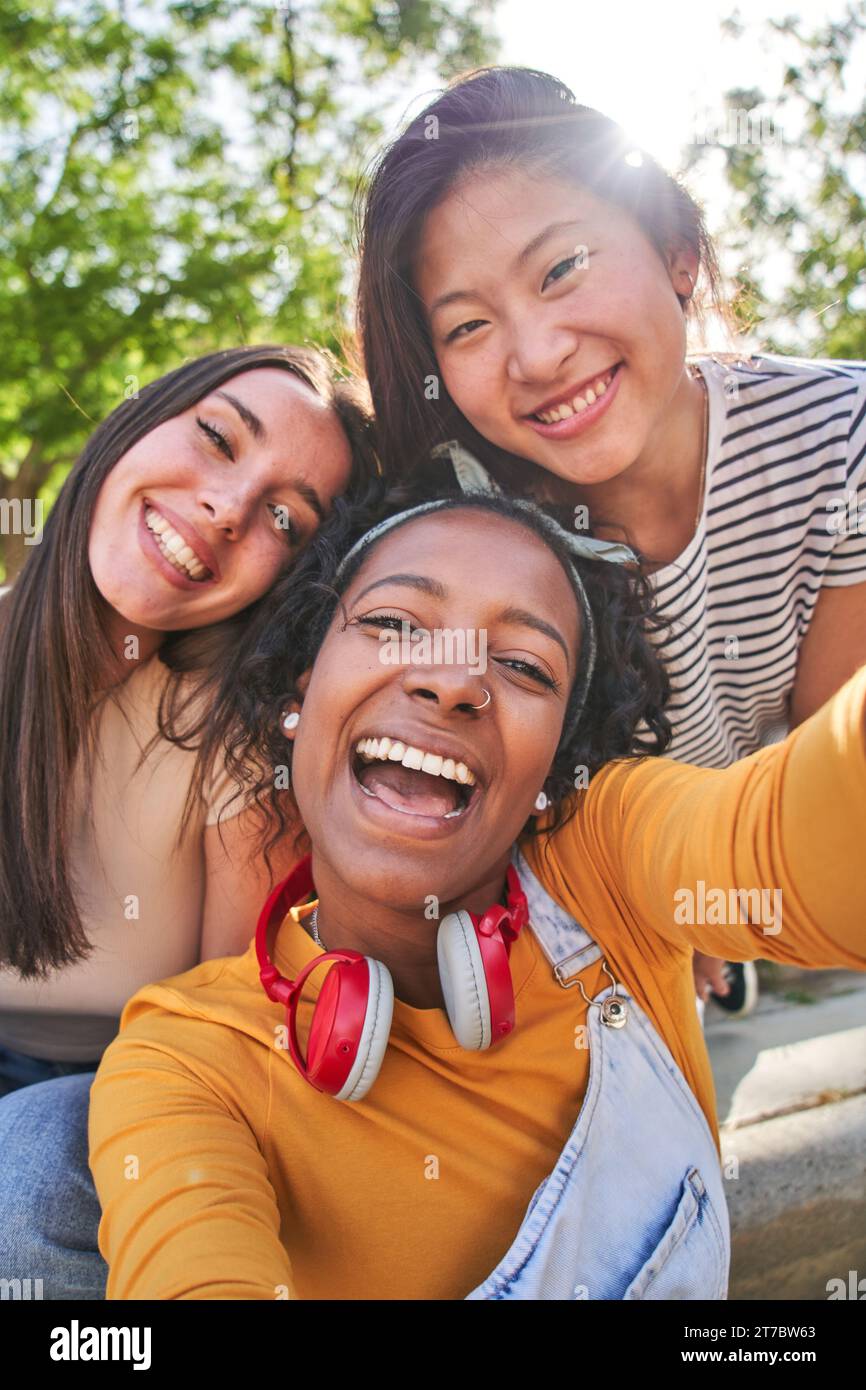 Vertical selfie three excited multicultural cheerful young women outdoor. Female having fun looking. Stock Photo