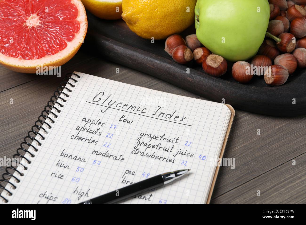 Notebook with products of low, moderate and high glycemic index, pen and food on wooden table, closeup Stock Photo