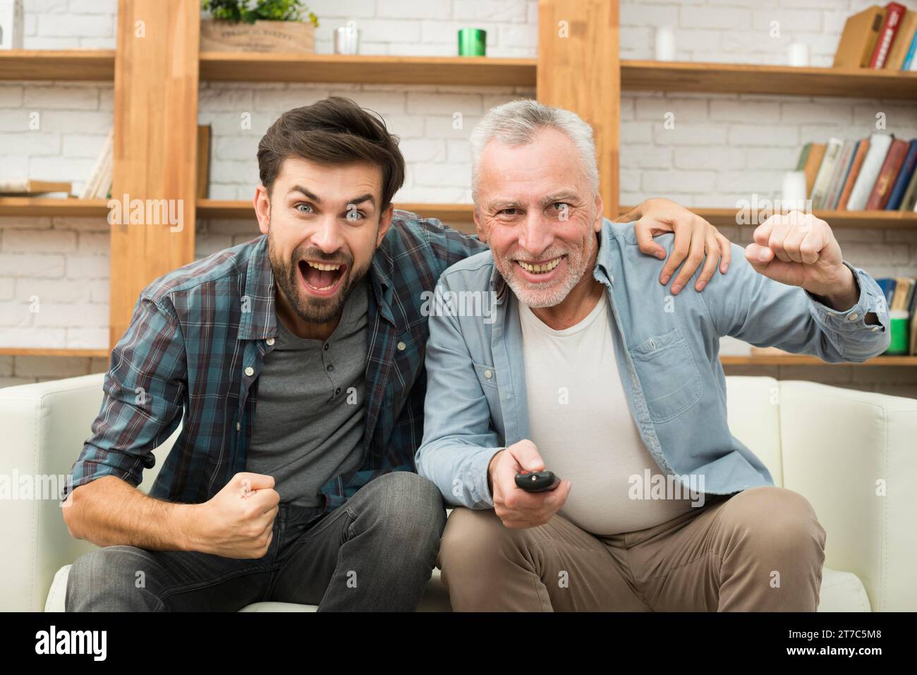 Aged happy man with remote control young crying guy watching tv sofa Stock Photo