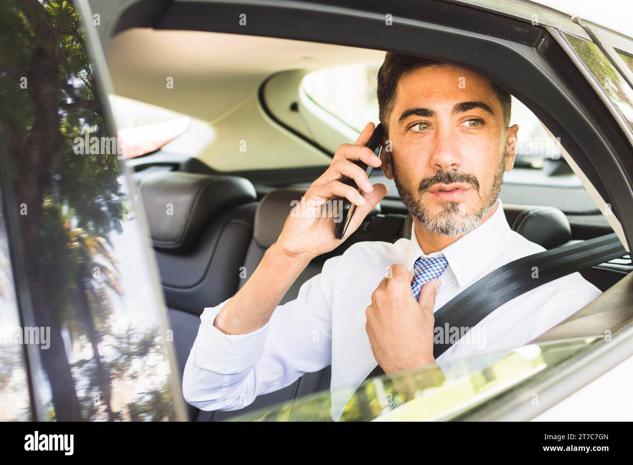 Modern man sitting car adjusting his neck tie talking mobile phone Stock Photo