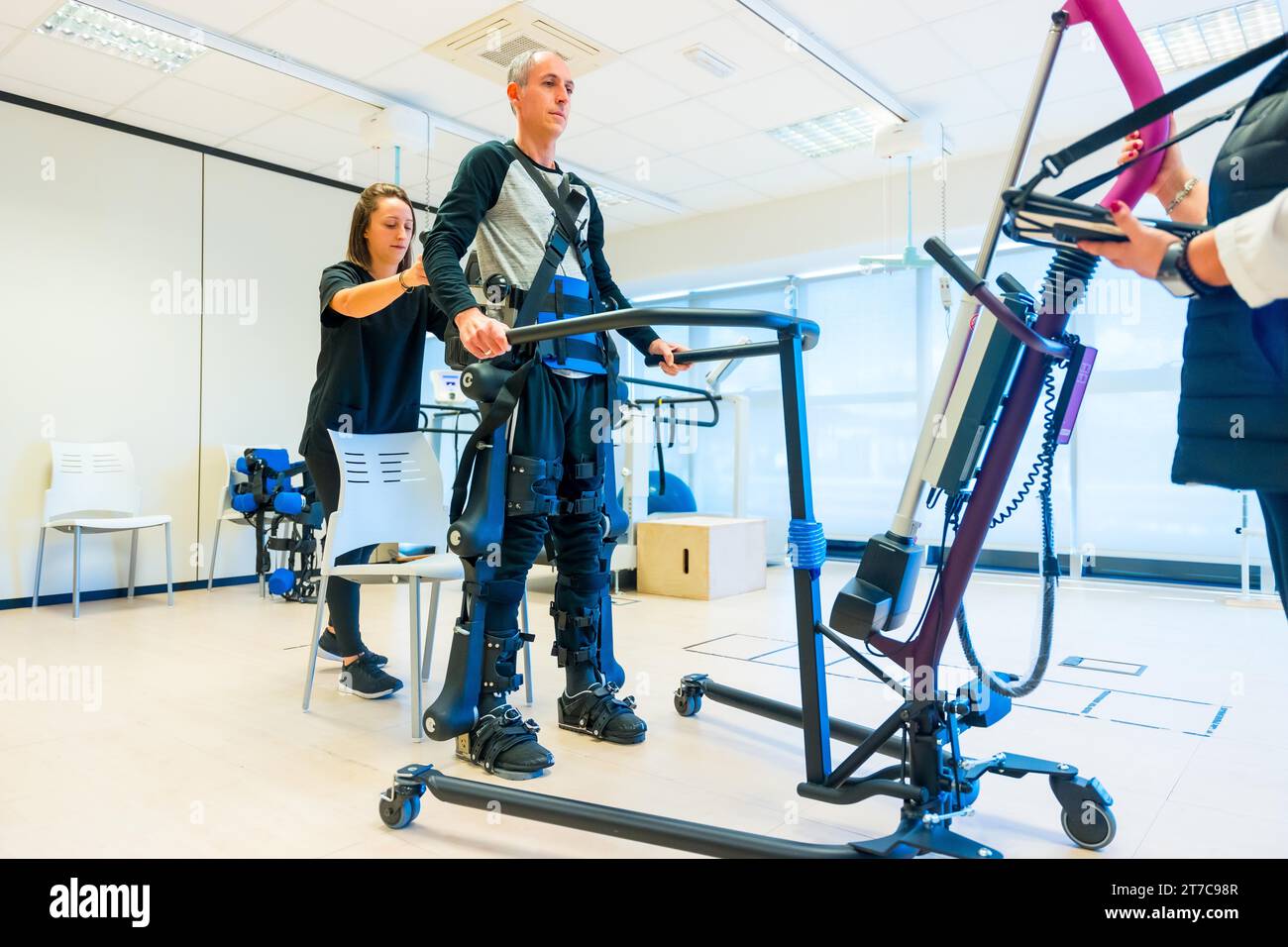 Mechanical exoskeleton. Female physiotherapy medical assistant lifting disabled person with robotic skeleton. Futuristic rehabilitation Stock Photo