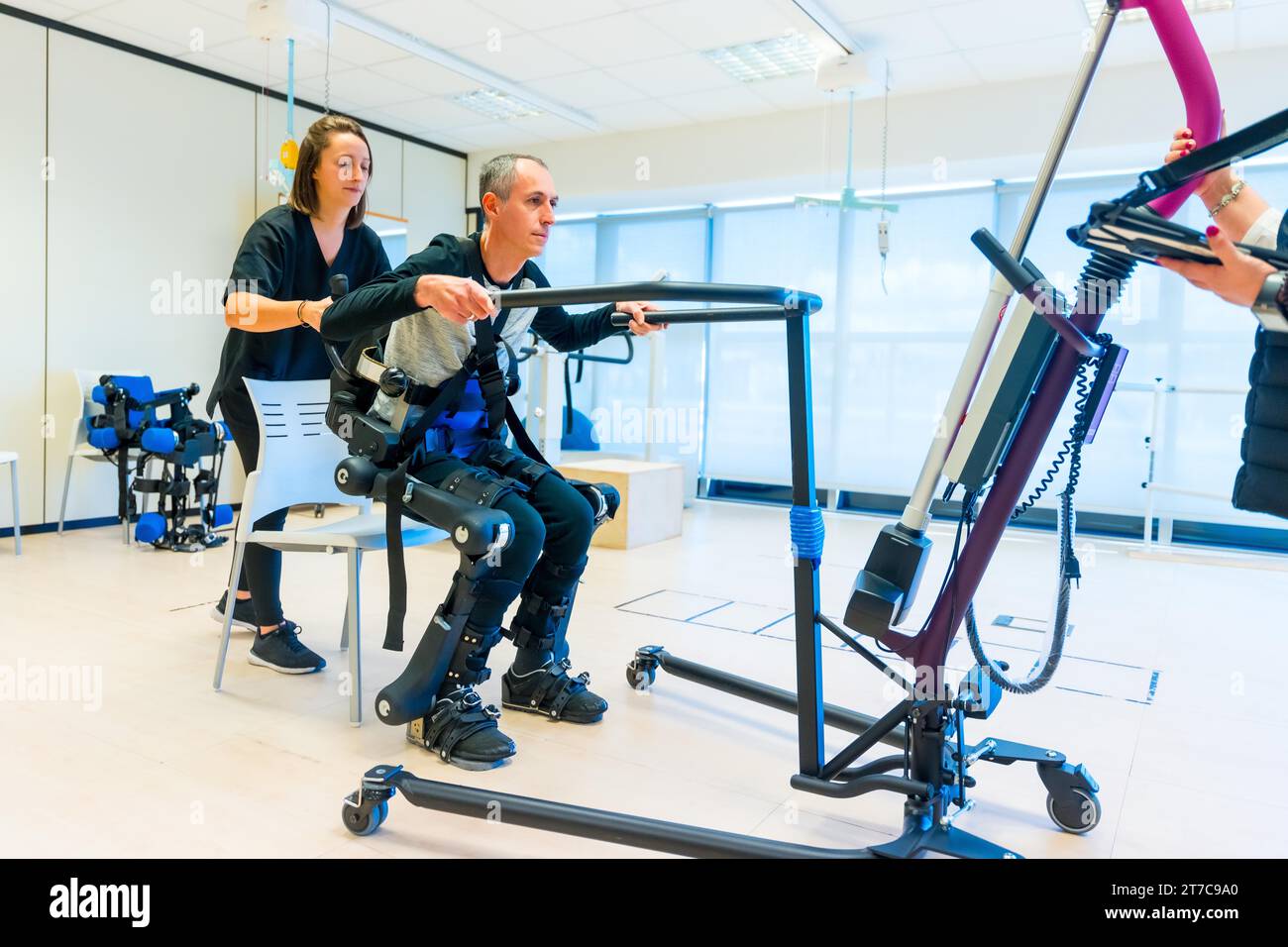 Mechanical exoskeleton. Female physiotherapy medical assistant lifting disabled person with robotic skeleton. Futuristic rehabilitation Stock Photo