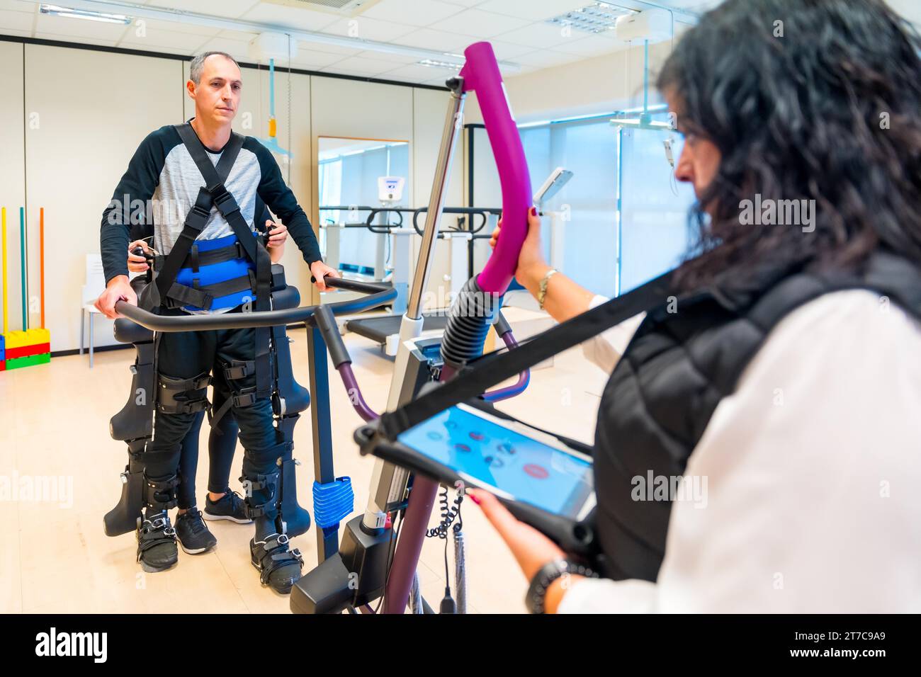 Mechanical exoskeleton. Female physiotherapy medical assistant with disabled person lifted with robotic skeleton. Futuristic rehabilitation Stock Photo