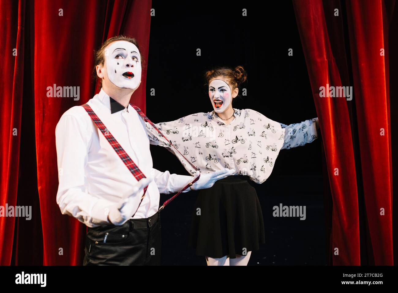 Happy female mime looking male mime holding suspender stage Stock Photo