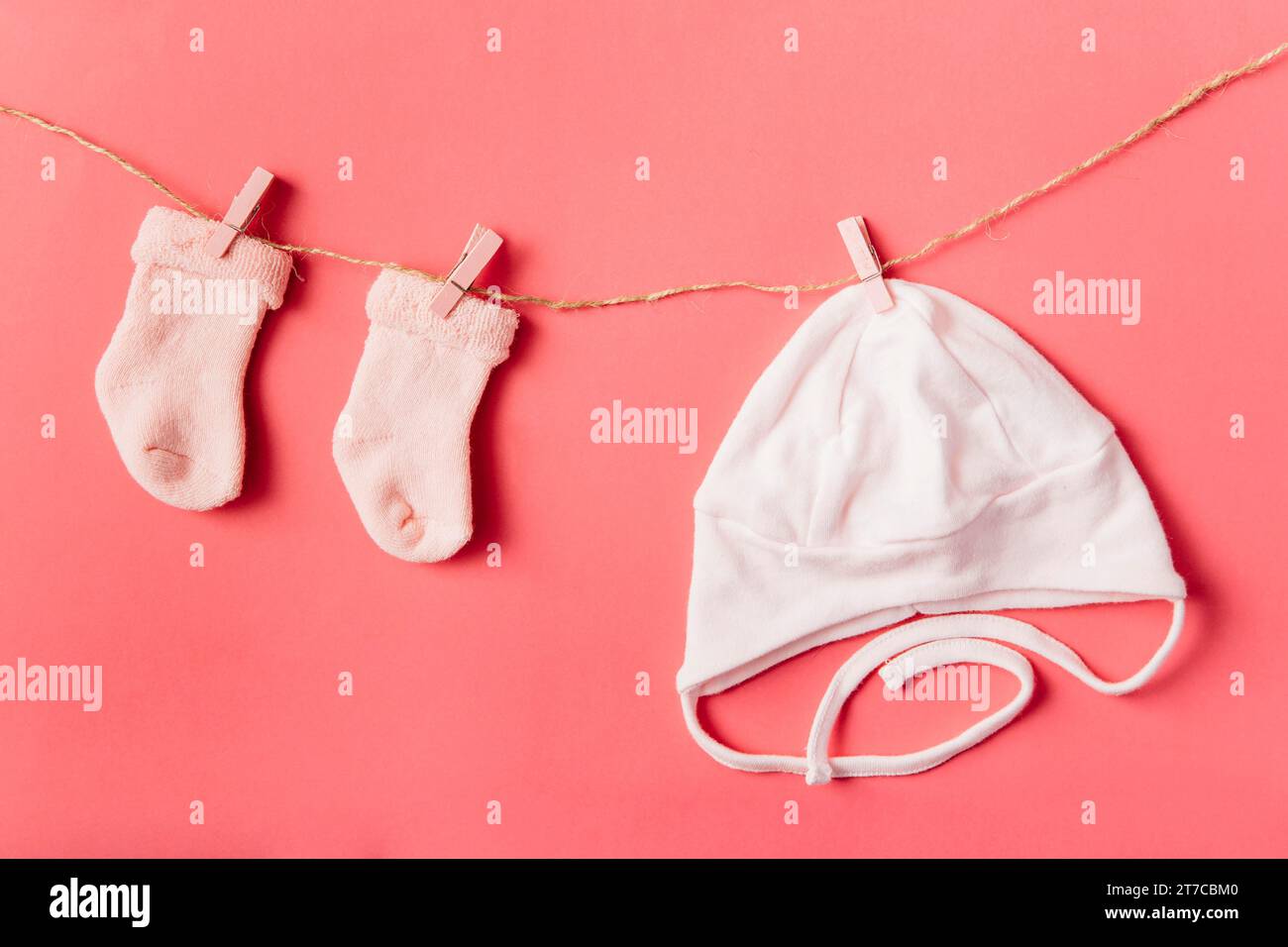 Pair baby s sock cap hanging with clothespin string against colored backdrop Stock Photo