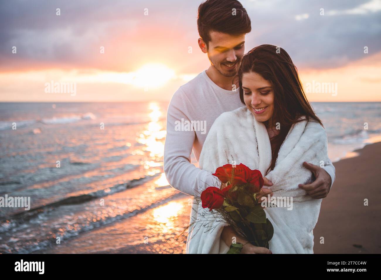 Smiling couple walking beach with bouquet roses sunset Stock Photo