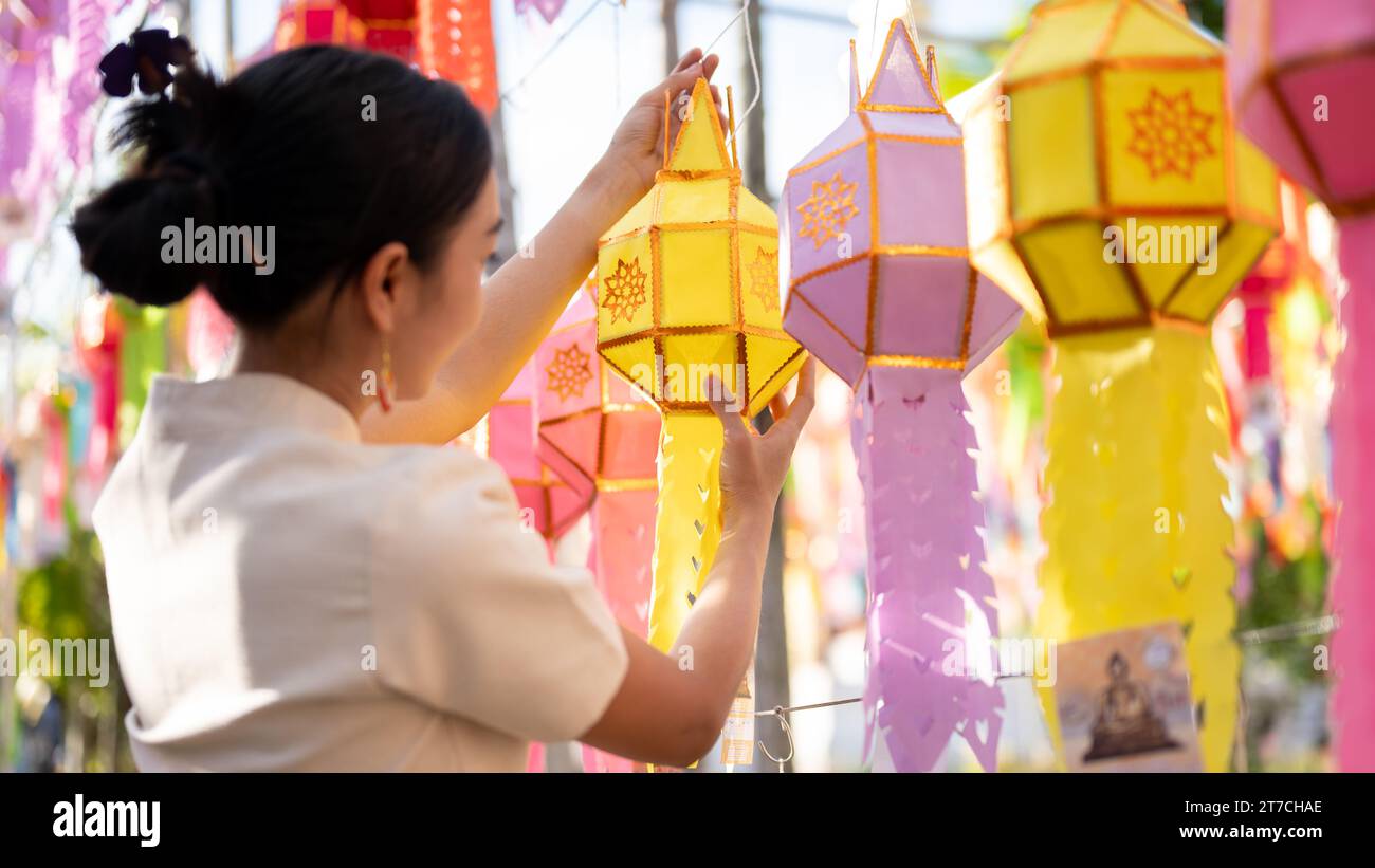 A beautiful and happy Thai-Asian woman is hanging a paper lantern and enjoying YI Peng or Loy Krathong festival at a temple in Chiang mai. Thai-Lanna Stock Photo