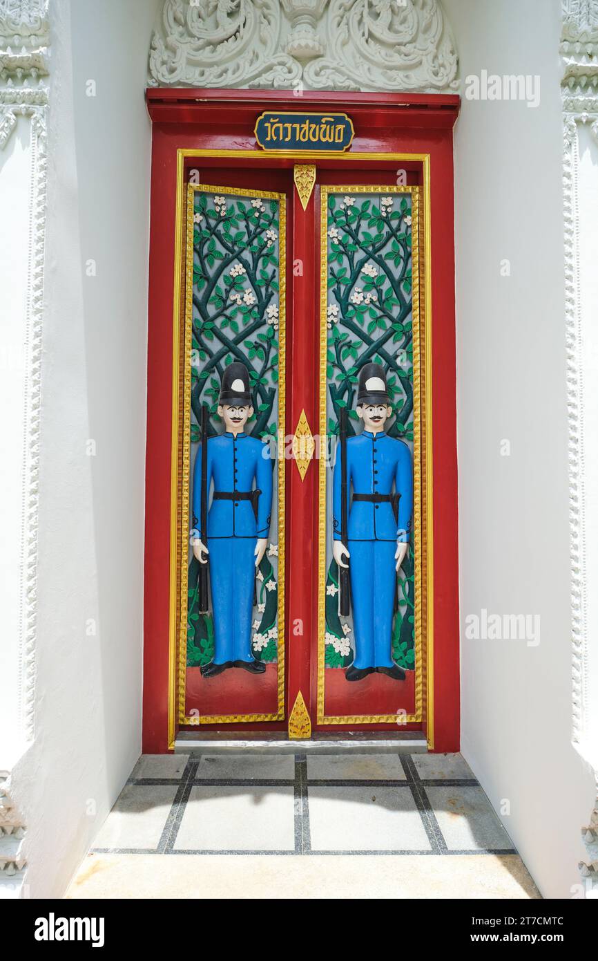 Two high relief guard figures adorn a door, done to look like traditional British Bobbies in blue uniform and high helmet, hat. At Wat Ratchabophit Sa Stock Photo
