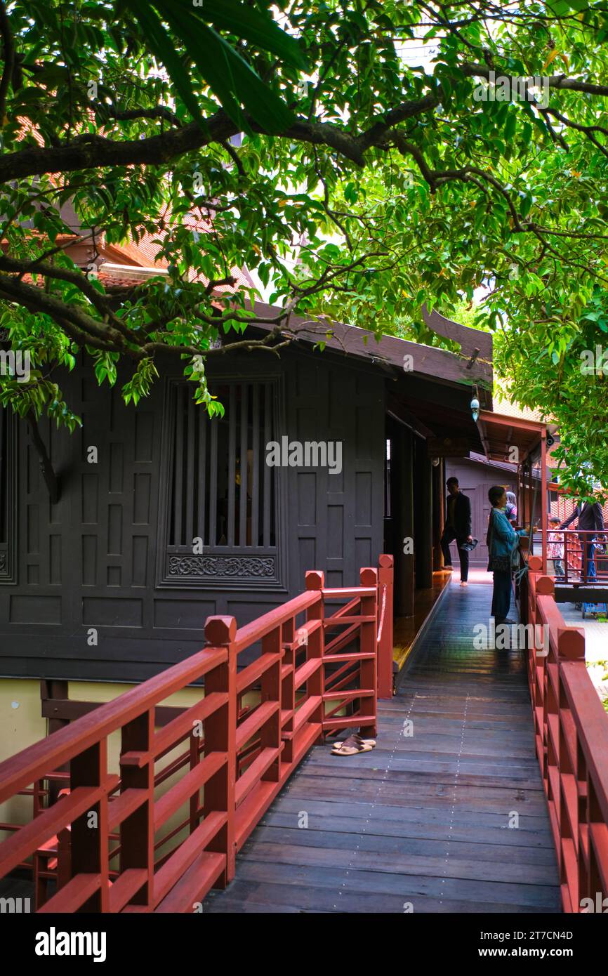 A wooden, red railing on a raised walkway that is used to connect some of the preserved houses. At the Suan Pakkad Palace traditional raised, wooden h Stock Photo