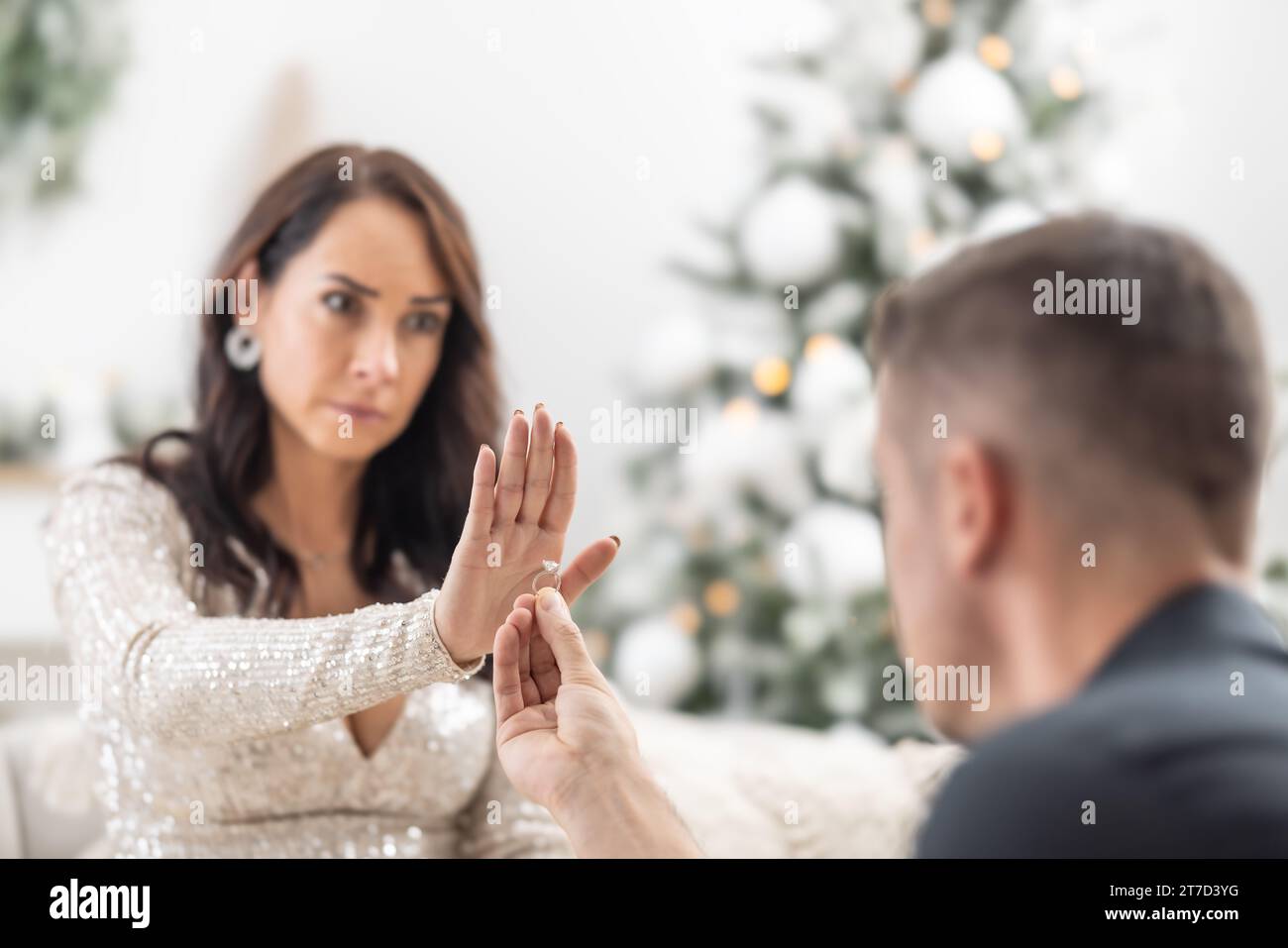 Woman declines a proposal to a man kneeing in front of her with a ring in his hand during Christmas. Stock Photo