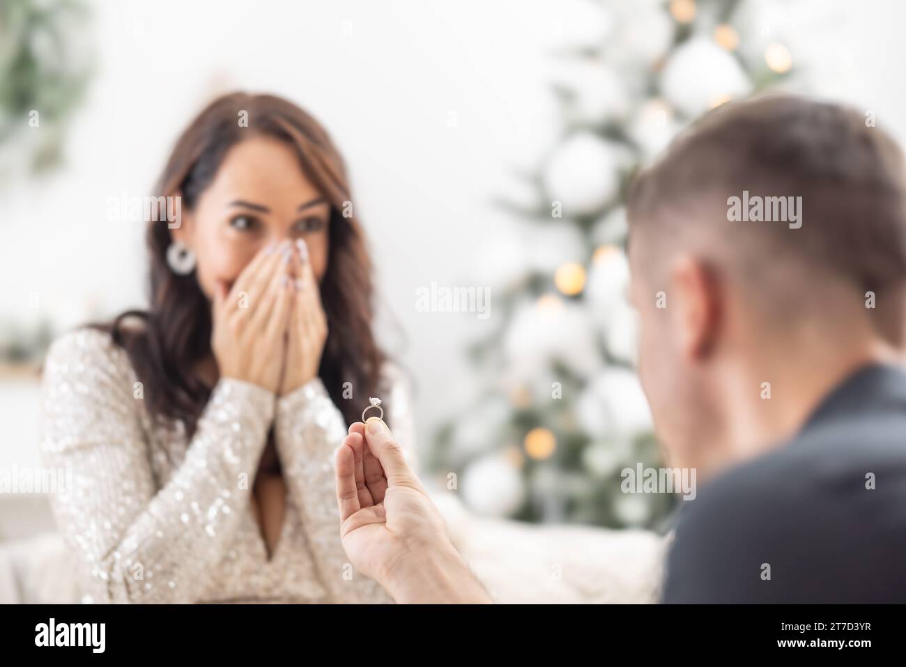 Christmas proposal by a man holding a ring in front of his surprised girlfriend. Stock Photo