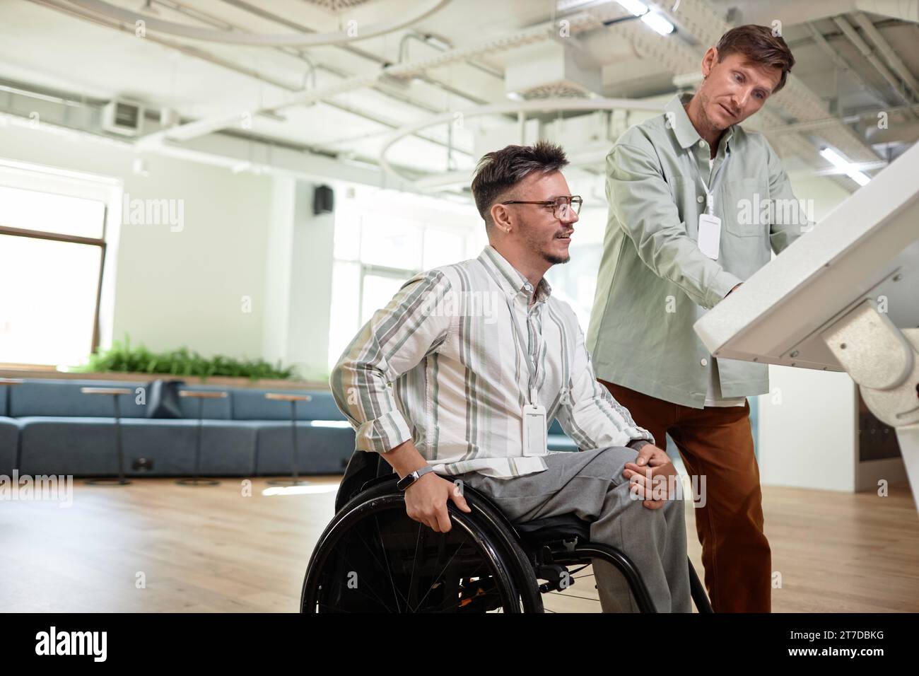 Young businessman helping man with disability using assistant computer Stock Photo