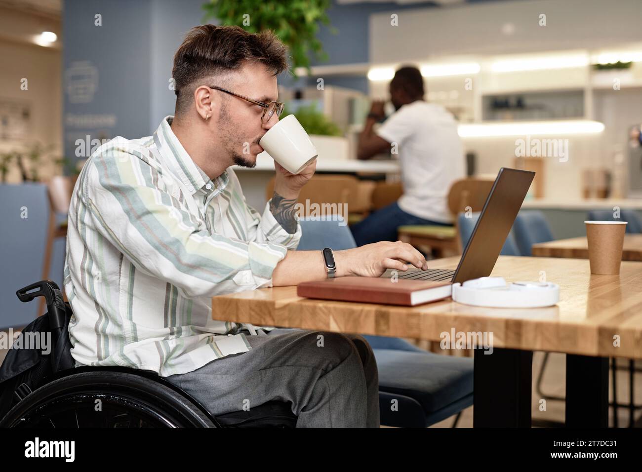Young businessman with disability drinking coffee while working online in cafe Stock Photo
